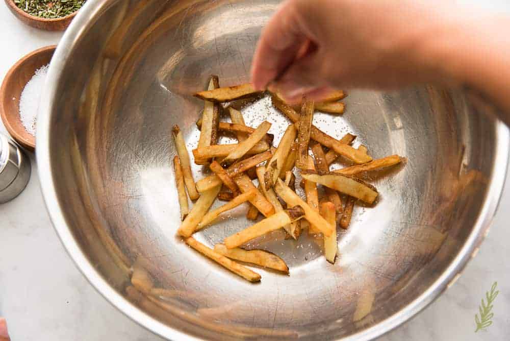 Sprinkling kosher salt onto the fries in a metal bowl