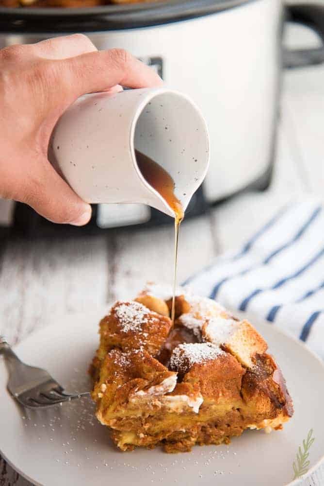 Pouring syrup over a plated portion of Pumpkin Cream Cheese Slow Cooker French Toast Casserole