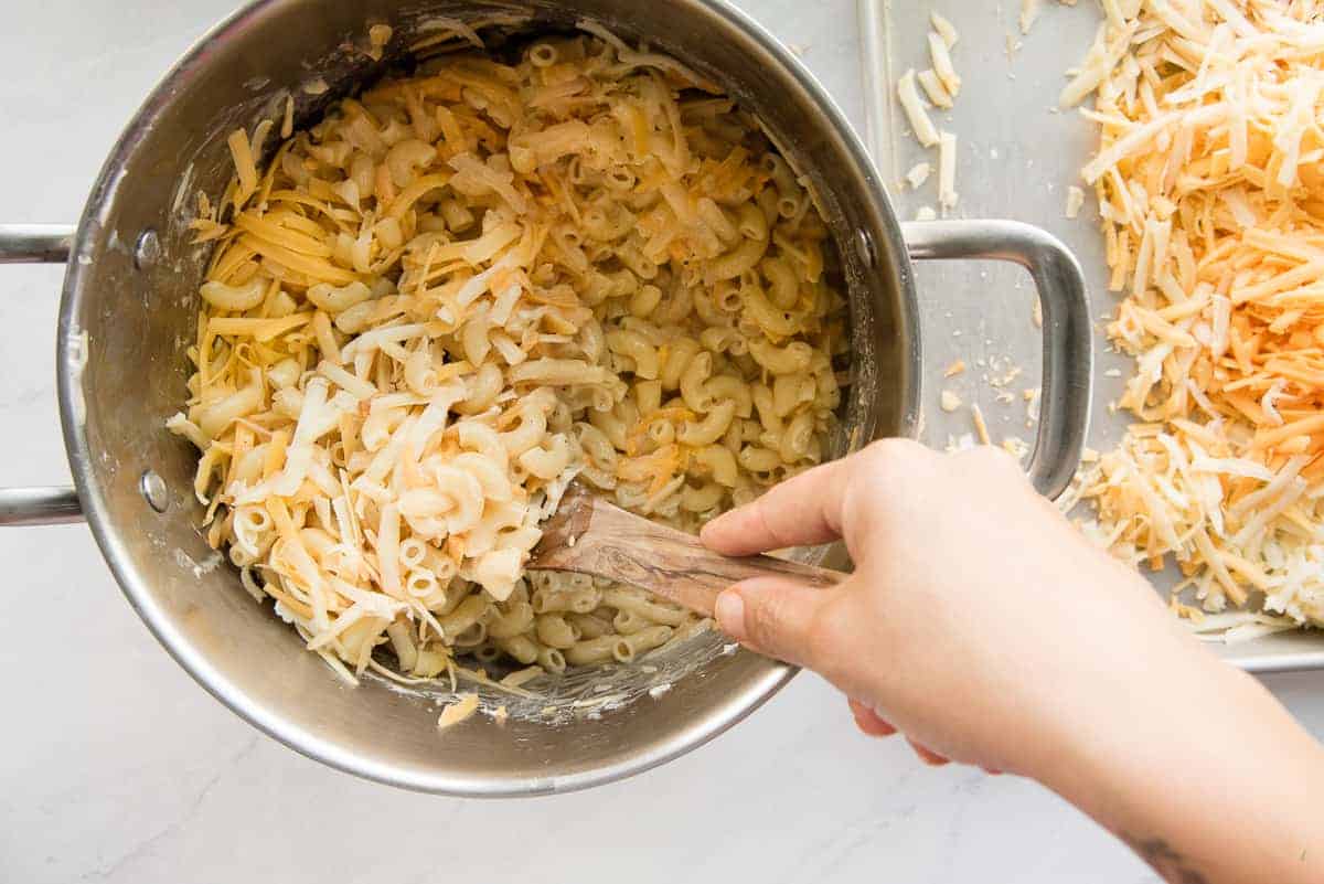 The shredded cheese is folded into the macaroni mixture in a silver pot.