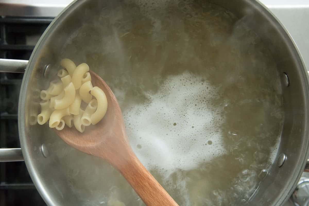 A spoon lifts the pasta from the boiling water to show how plump it is.