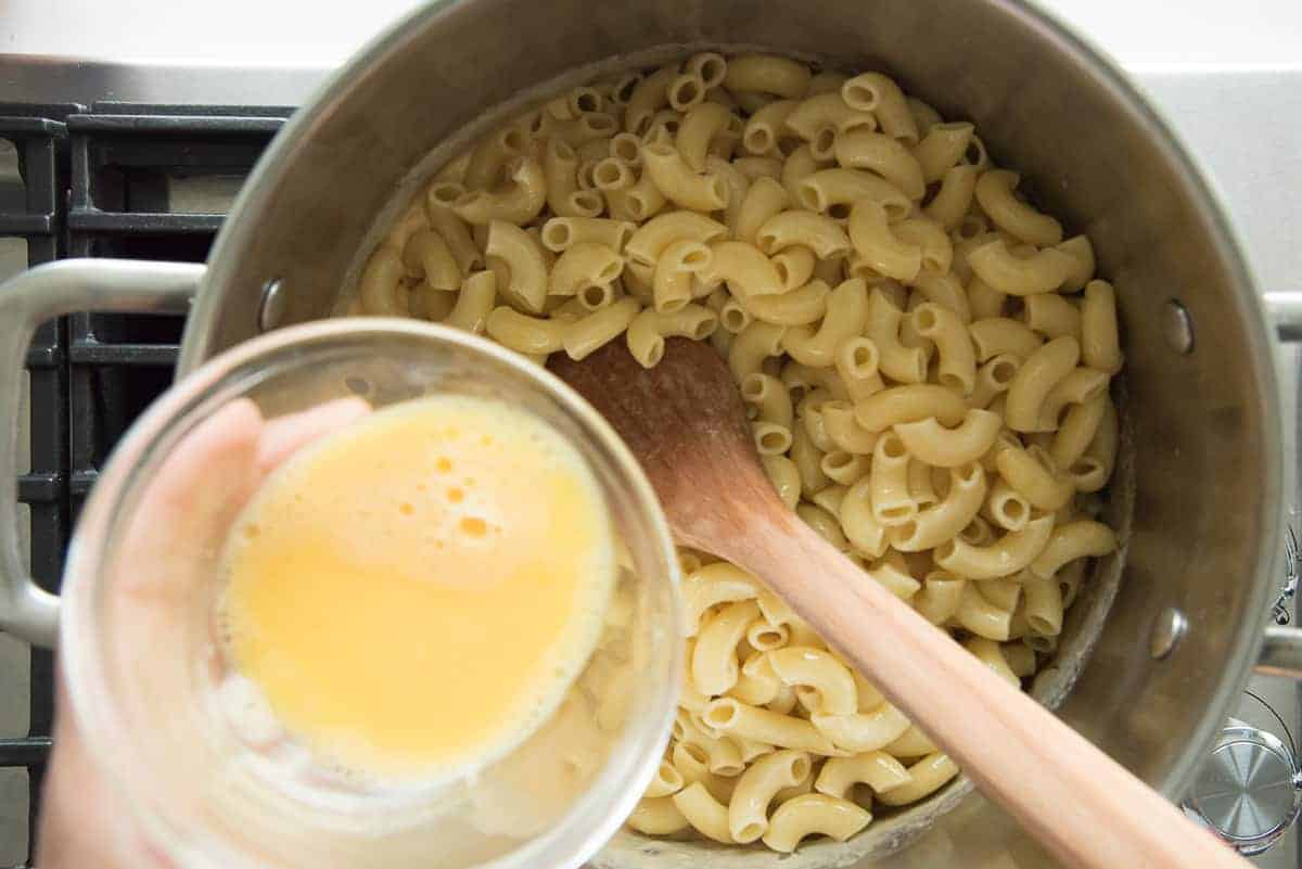 The beaten egg is added to the pasta in the pot.