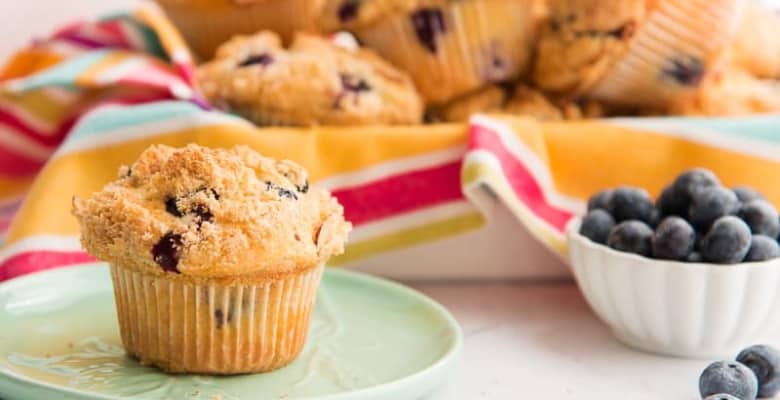 A single muffin sits on a green plate. A bowlful of berries sits beside it.