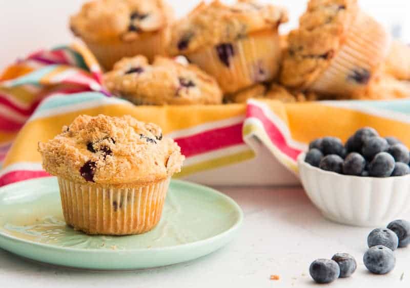 A single Blueberry Almond Streusel muffin sits on a green plate. A bowlful of berries sits beside it.