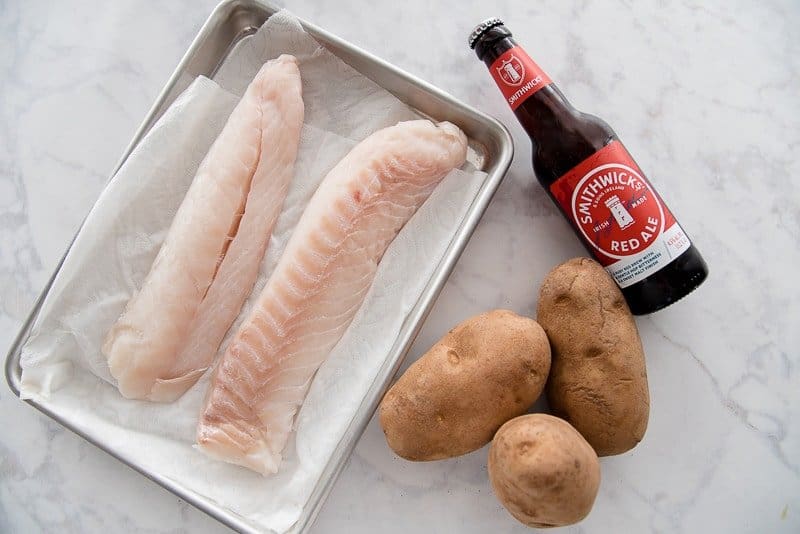 The ingredients need to make Fish and Chips on a white countertop.