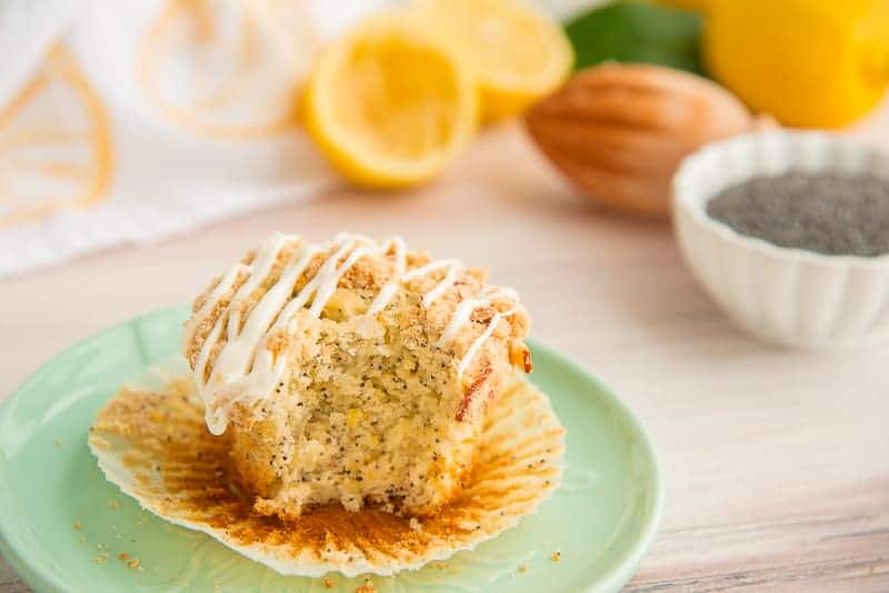 A huge bite has been taken out of a lemon poppy seed muffin. It sits on its white wrapper on a mint green plate