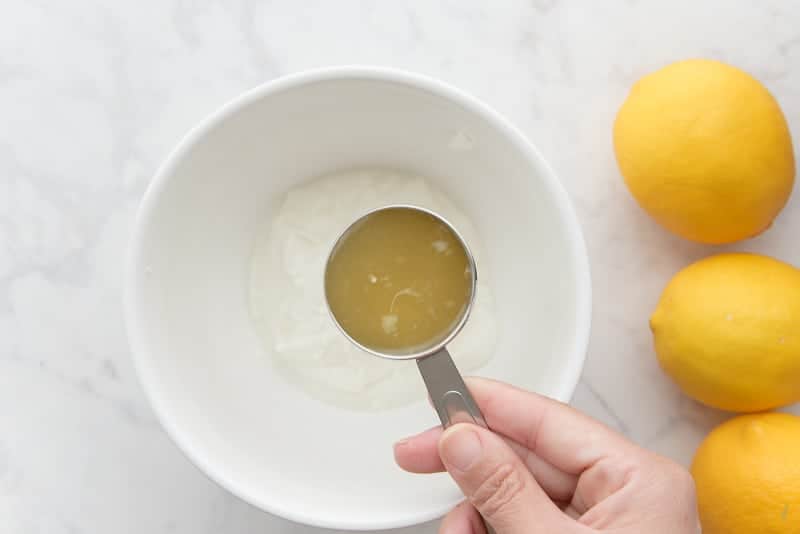 A hand adds the lemon juice to the greek yogurt, which is in a white bowl