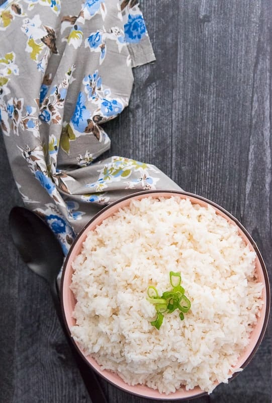 A bowl of Arroz Blanco (Steamed White Rice) on a dark background with a grey floral napkin next to it