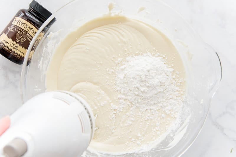 The cornstarch is mixed into the cheesecake batter by a white electric hand mixer