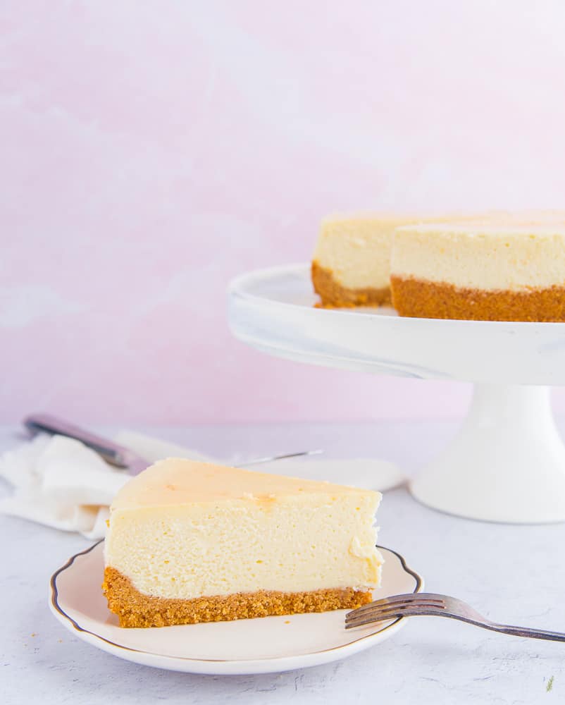 A portrait image of a slice of Classic Cheesecake with Graham Cracker Crust on a white plate