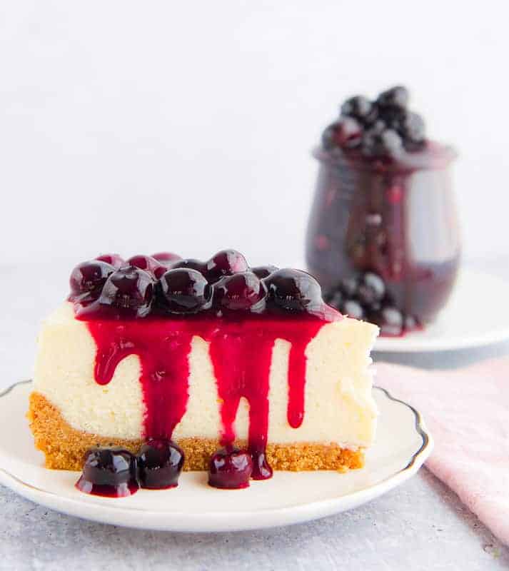 A slice of cheesecake is topped with Blueberry Ginger Dessert Topping