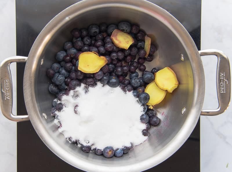 Blueberries, ginger slices, and sugar are added to a pot