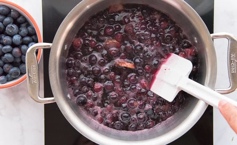 Blueberries, ginger slices, and sugar are boiled together with water in a pot