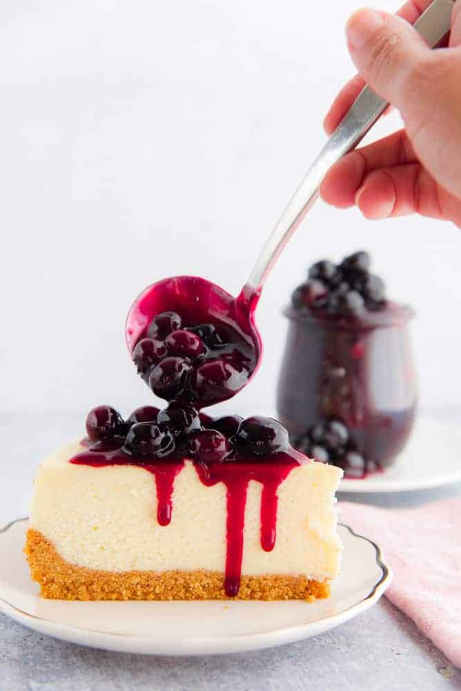A spoonful of Blueberry Ginger Dessert Topping is poured over a slice of cheesecake