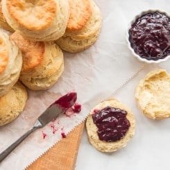 An overhead image of a stack of buttermilk biscuits and jam on a wooden board