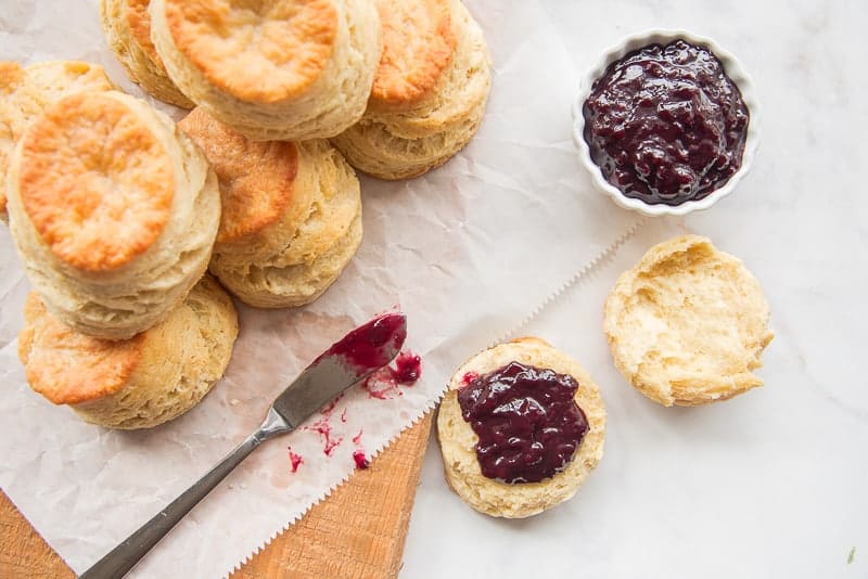 An overhead image of a stack of buttermilk biscuits and jam on a wooden board