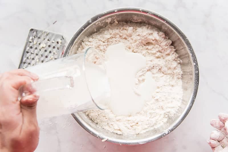 A pitcher of buttermilk is poured into the flour-butter mixture