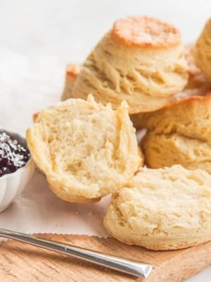A stack of Buttermilk Biscuits, blackberry jam and a knife sit on a wooden board