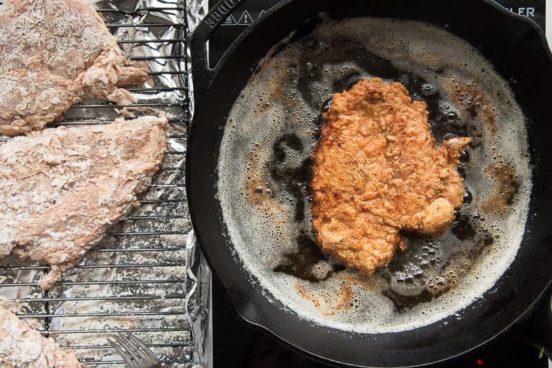 A piece of Chicken Fried Chicken is finished frying in a black cast iron skillet