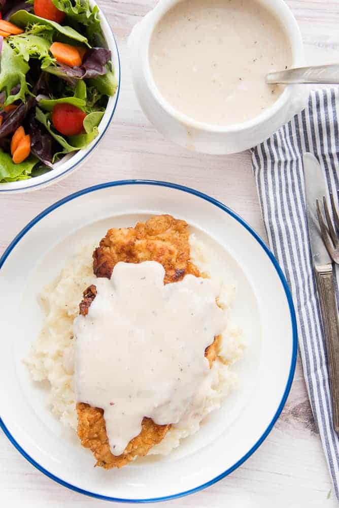 A portrait image of a blue-rimmed plate with mashed potatoes and Chicken Fried Chicken with Pan Gravy
