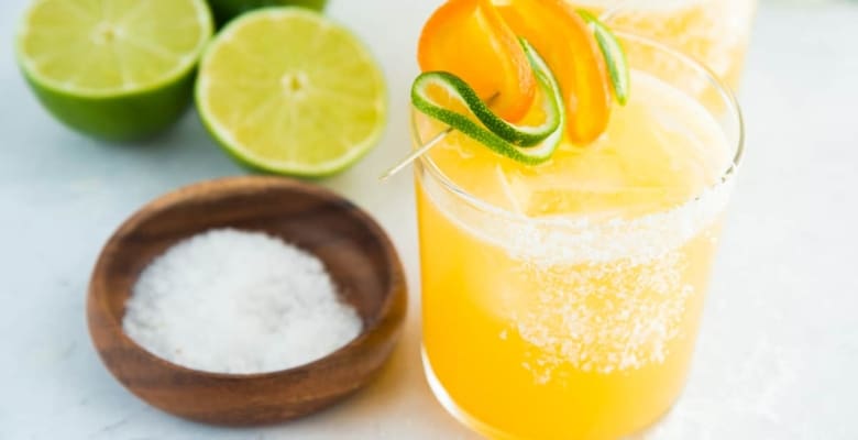 An up close image of a salt-rimmed glass filled with Chispa Margarita. A bowl of salt sits next to the cocktail