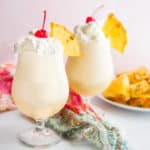 Two glasses filled with Classic Piña Colada cocktail and topped with whipped cream and a cherry
