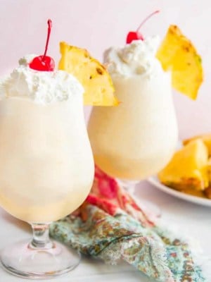 Two glasses filled with Classic Piña Colada cocktail and topped with whipped cream and a cherry