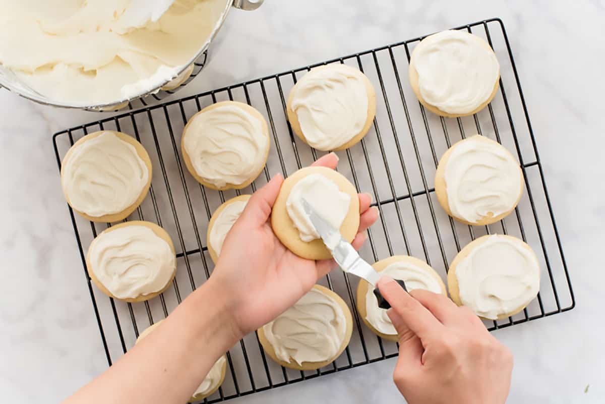 A hand smoothing frosting over a Soft Sugar Cookies with Cream Cheese Frosting