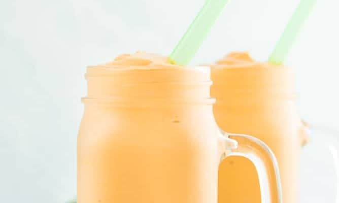 A portrait image of two glass jars filled with Sense & Edibility's 4 Ingredient Fruit and Yogurt Smoothie a green straw is in the smoothie and a green napkin sits next to them