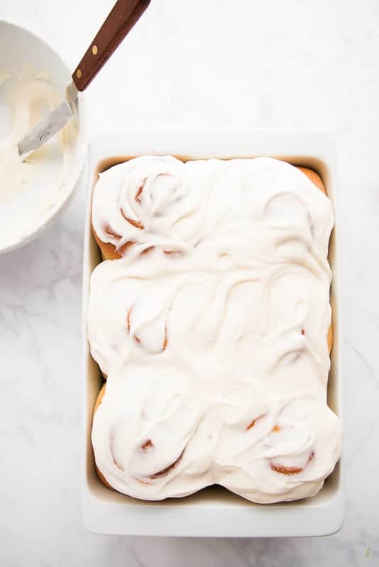 A white casserole dish filled with Cinnamon Rolls that have been iced with Cream Cheese Icing.
