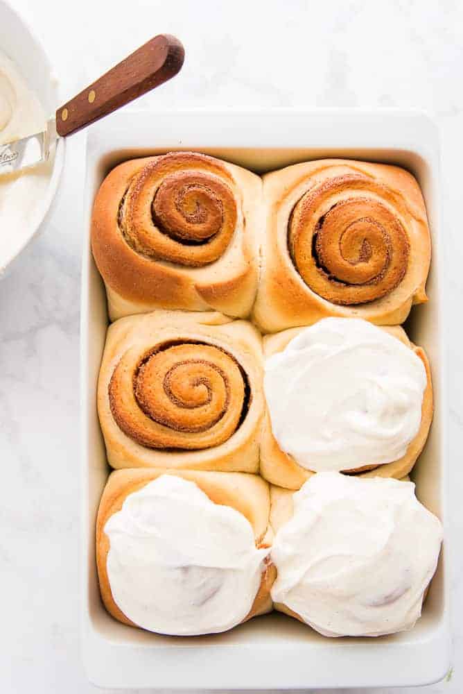 A portrait image of a pan of baked cinnamon rolls. Half of the rolls have been iced