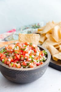A tortilla chip sticking out of a wooden bowl filled with pico de gallo