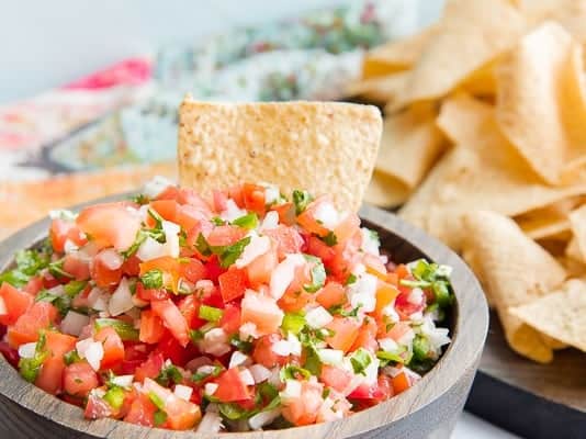 A tortilla chip sticking out of a wooden bowl filled with pico de gallo