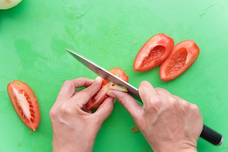 A knife is removing the membrane and seeds from the tomatoes