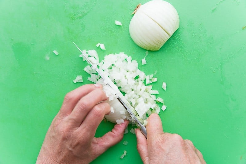 A white onion is being diced on a green cutting board