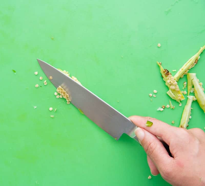 A knife scrapes off jalapeño pepper seeds