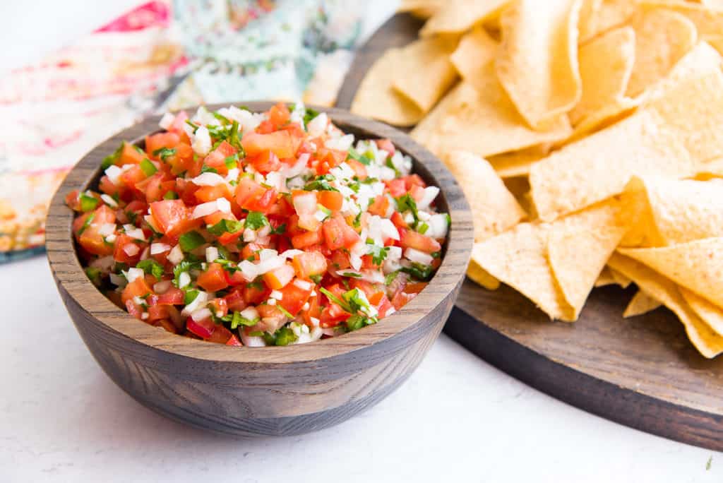 A sideview image of a wooden bowl filled with pico de gallo