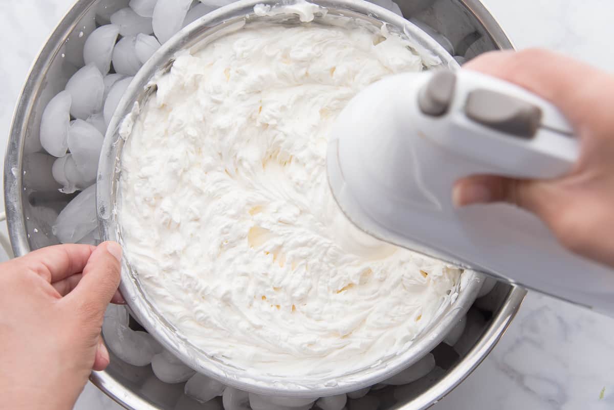 Heavy cream is whipped in a stainless steel bowl by an electric hand mixer