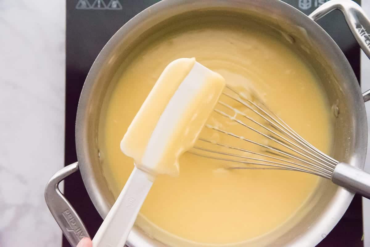 A spatula tests to make sure the custard is thick. A line made by a finger is created on the spatula through the custard