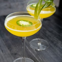 A long image of two Pineapple Jalapeno Margaritas in long stem coupe glasses