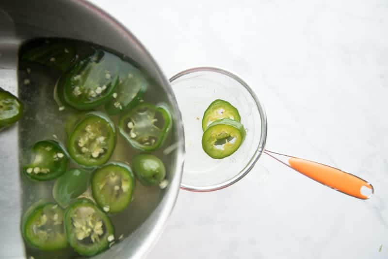 The jalapeno simple syrup is poured through a sieve to strain off the jalapeno slices