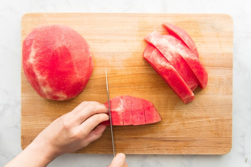 Watermelon is being cut on a wooden cutting board