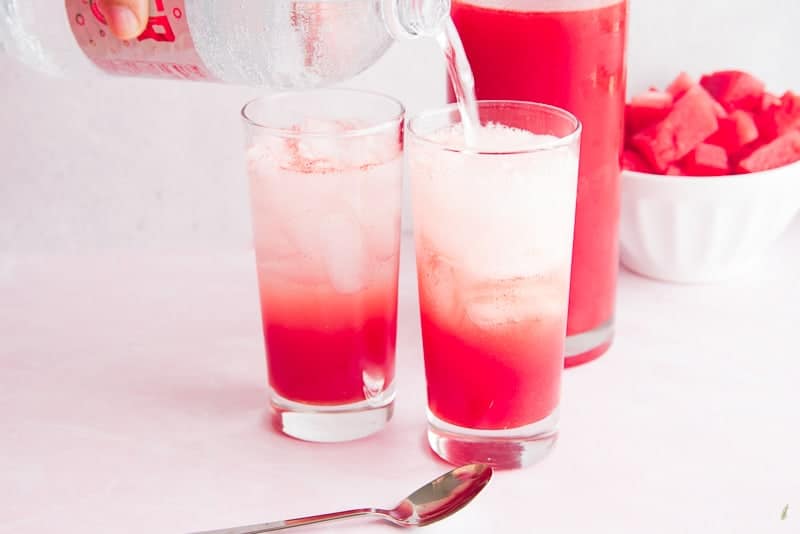 Seltzer water is poured into a glass filled with ice cubes and watermelon simple syrup