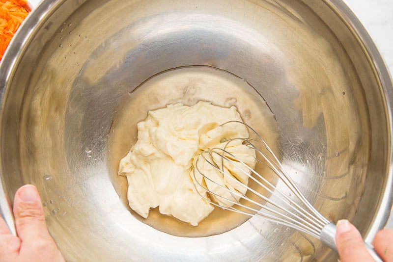 A whisk is used to mix the apple cider vinegar and mayonnaise together in a large metal mixing bowl