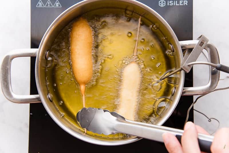 Tongs are used to flip the Pancakes and Sausage on a stick in the frying oil