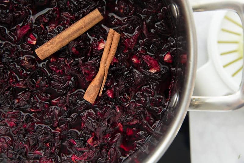 The hibiscus flowers and two cinnamon sticks are added to a pot of water before being boiled.