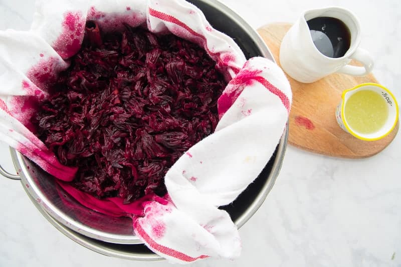 The steeped hibiscus flowers are in a white and red tea towel prepared to be strained.