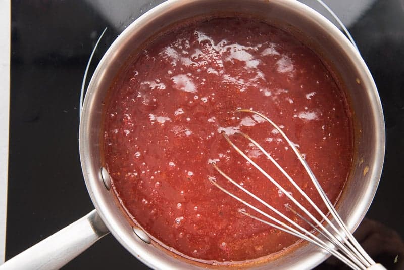 The BBQ sauce is simmering on a stove in a silver pot.
