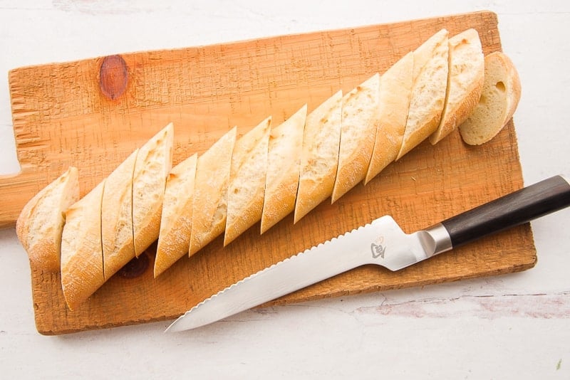 A loaf of bread is sliced on a brown wooden cutting board next to a serrated bread knife.