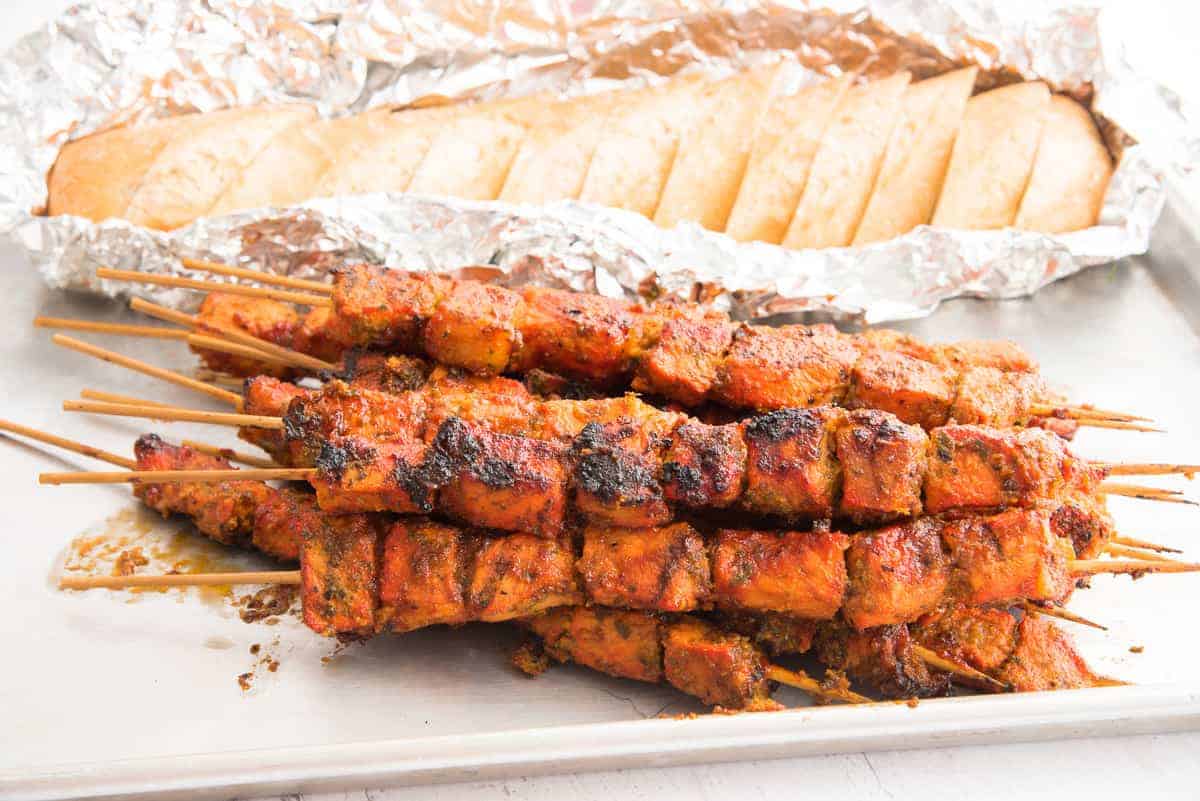 A horizontal image of a stack of Pinchos on a sheet pan in front of a loaf of sliced bread in foil