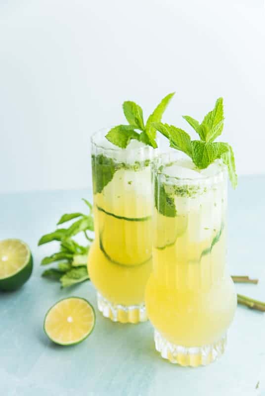 Portrait image of Two highballs of Puerto Rican Mojitos, sliced limes and mint sprigs lie around the glasses